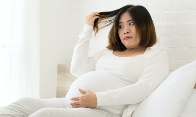 a pregnant woman dressed in white sits and holds out her hair as she looks as it