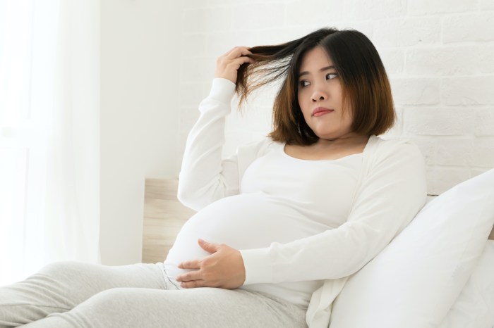 a pregnant woman dressed in white sits and holds out her hair as she looks as it