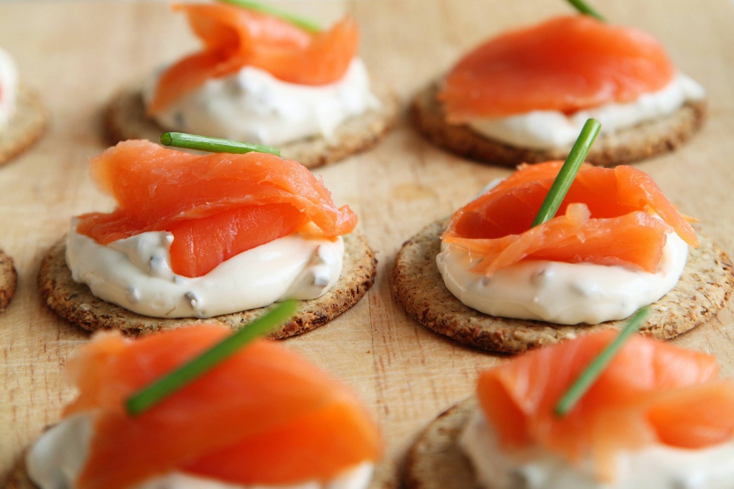 six crackers with cream cheese spread, salmon, and and herb garnish on a wooden counter