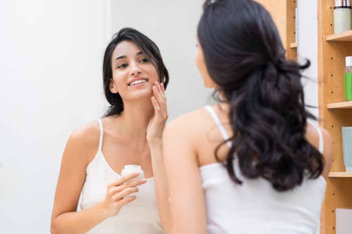 woman applying face lotion in bathroom