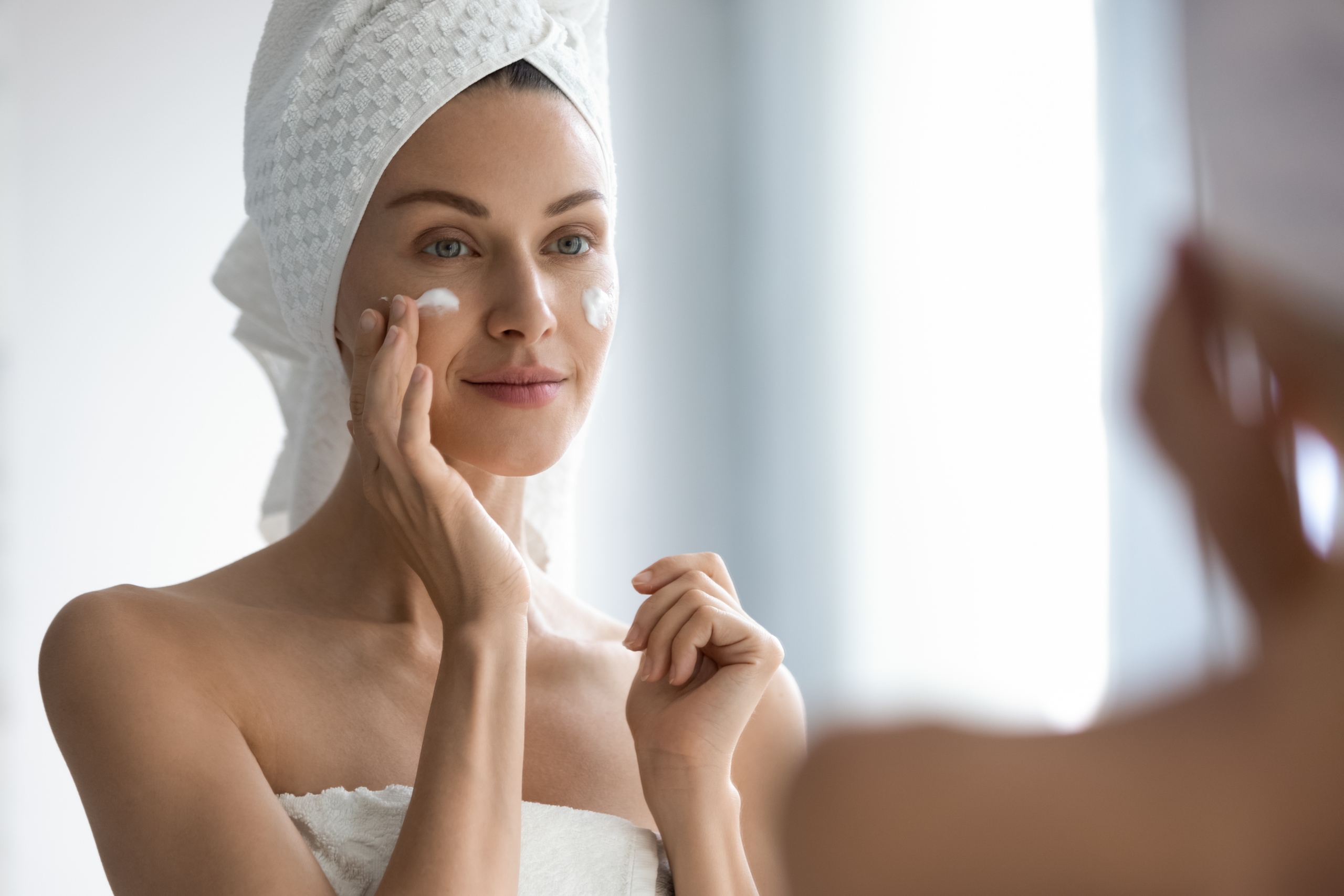 woman applying moisturizer in mirror