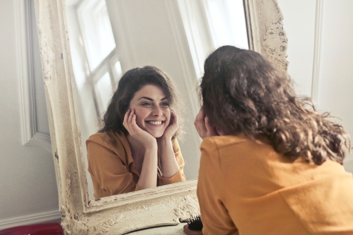 A woman smiling at her reflection in a mirror.