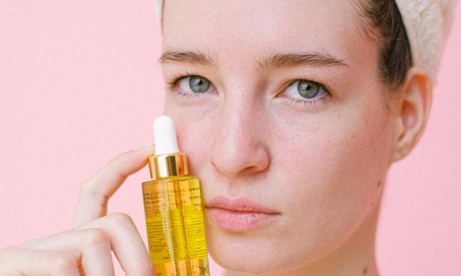 Woman holding up a bottle of serum to her face.