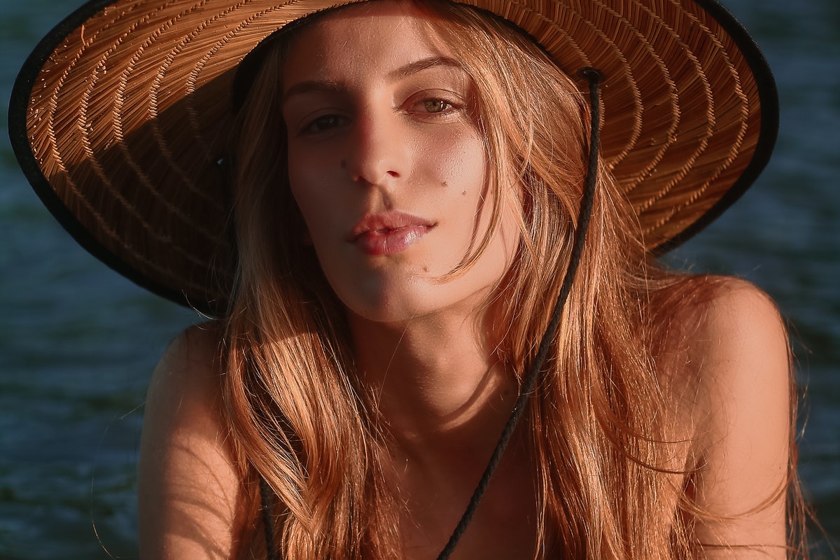 A woman wearing a straw sun hat with long, beachy, wavy hair.