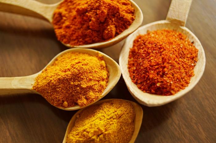 Different spices, like turmeric, in spoons laying on a table.