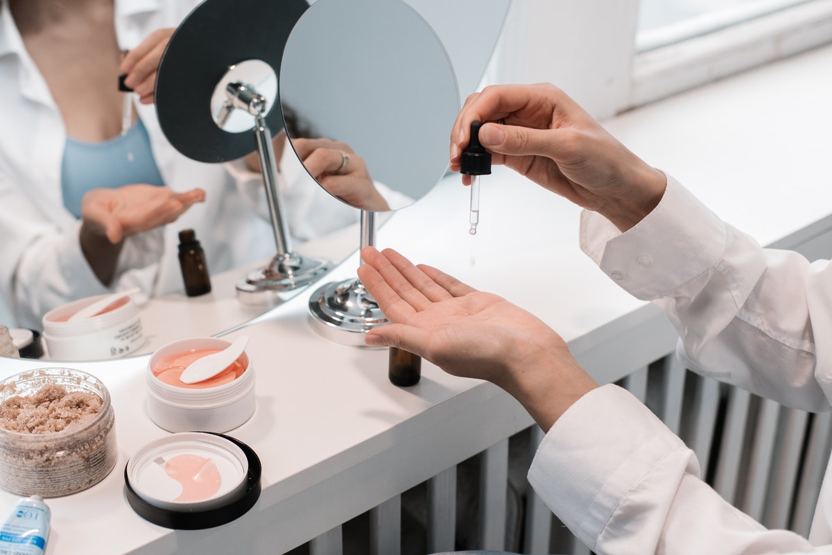 A woman dropping serum into one of her hands in front of a mirror where other beauty products are laid out.