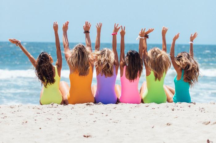 A group of females sitting on the beach facing the water so you see their backs and beachy hair.