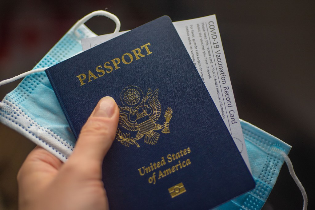 Person holding a passport, vaccination card, and mask