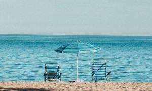 A beach umbrella in between 2 beach chairs.