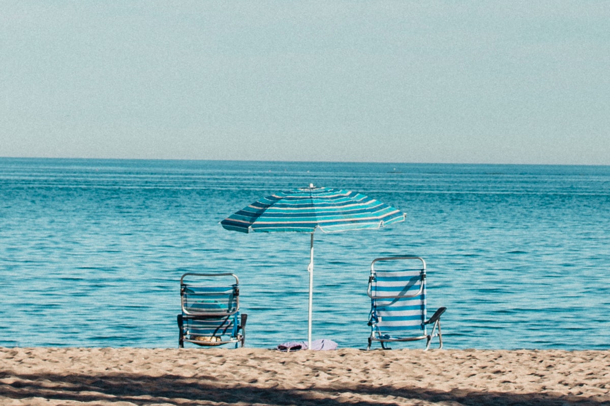 A beach umbrella in between 2 beach chairs.