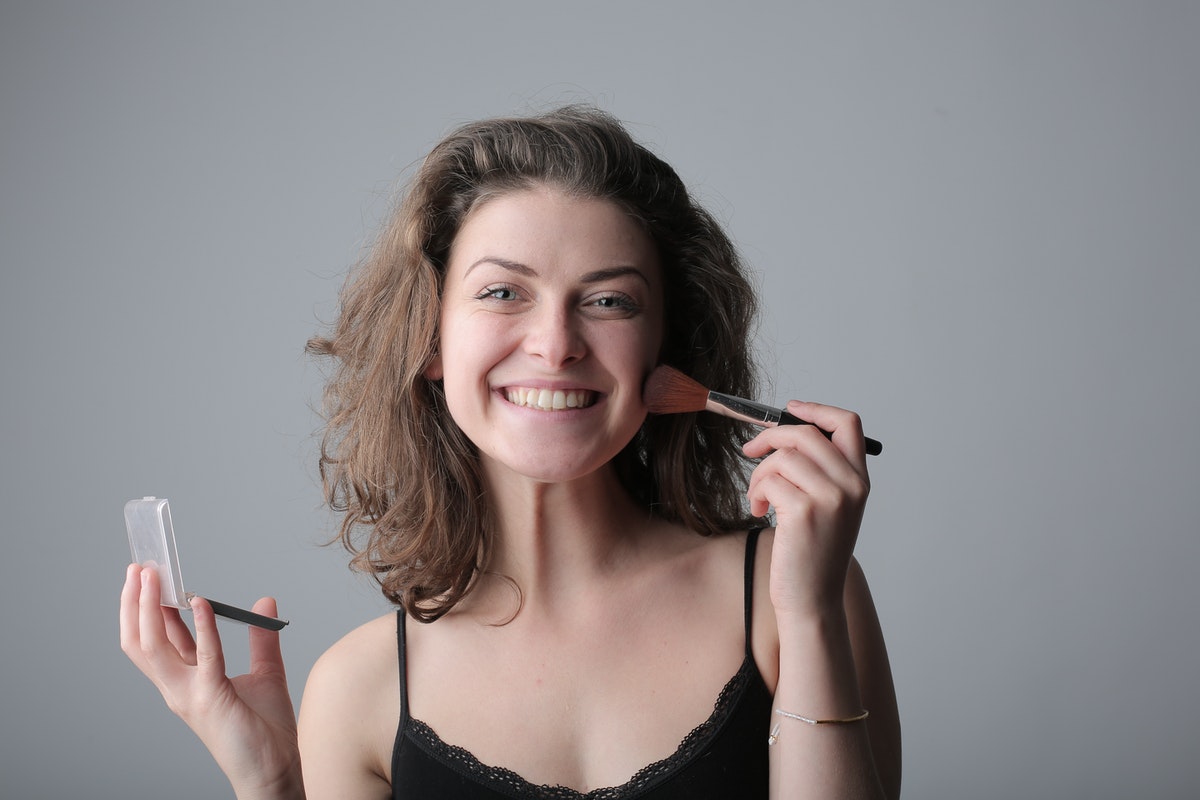 A woman smiling as she puts on her makeup.
