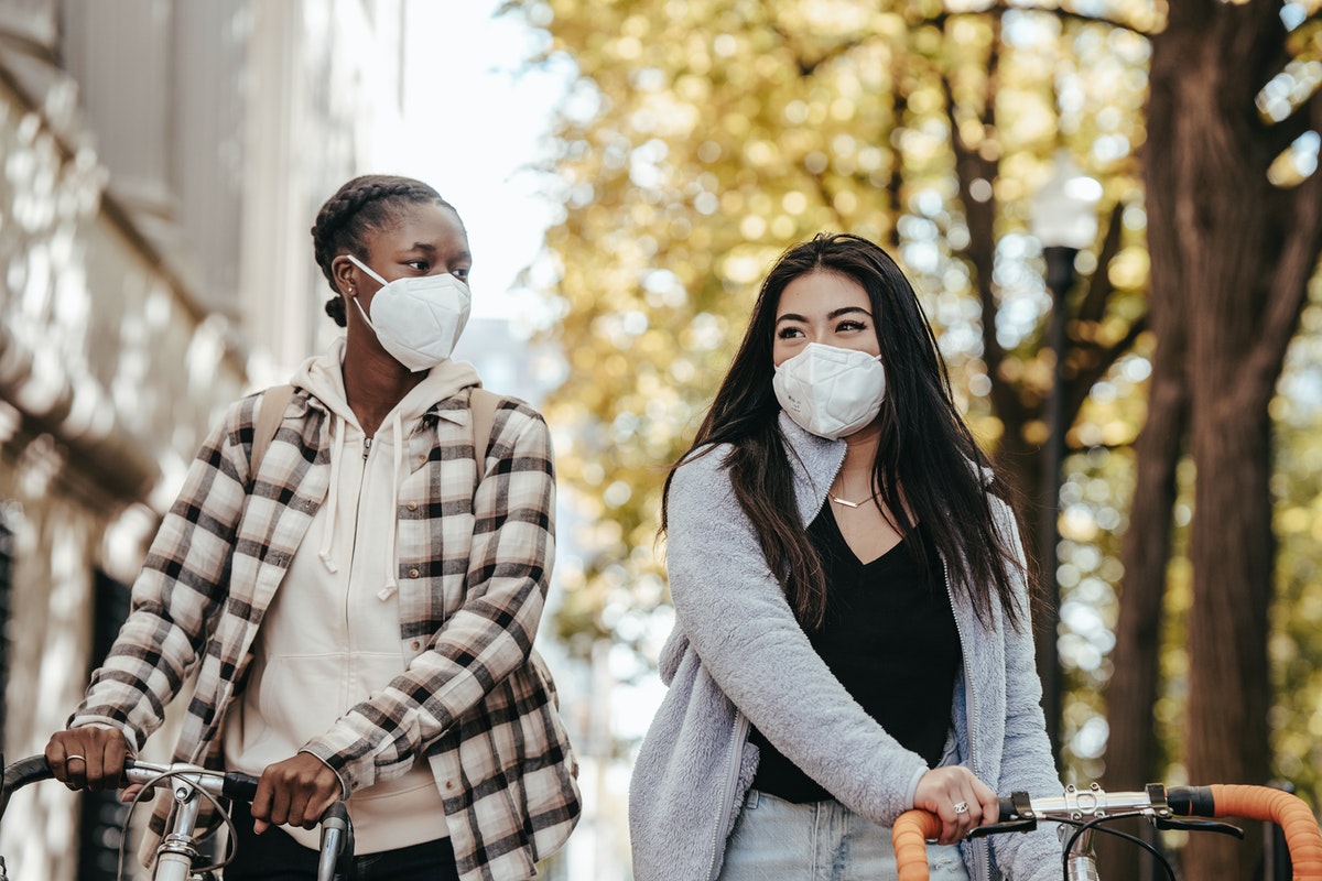 Two woman walking their bikes while wearing face masks.