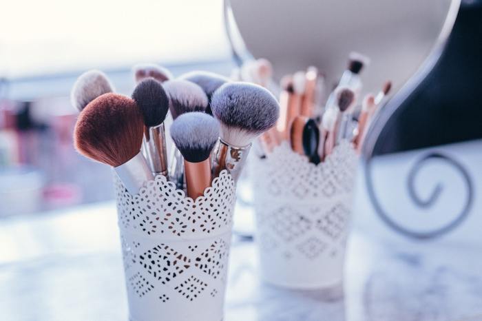Two cups of makeup brushes sitting on a table.