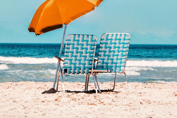 A beach umbrella next to a few empty beach chairs.
