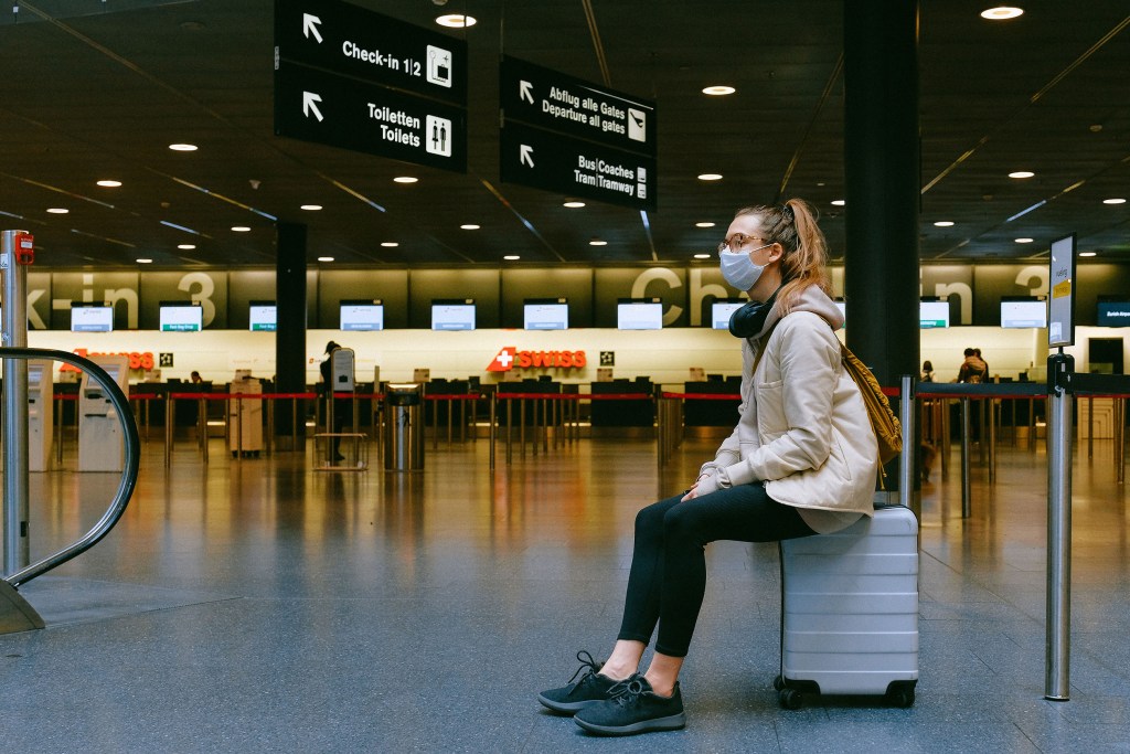 Woman wearing a mask sitting on suitcase in the airport