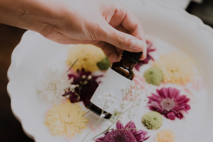 person holding a bottle of essential oil over a white basin with flowers