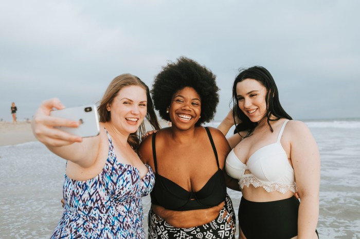Curvy women in swimsuits taking selfie on beach