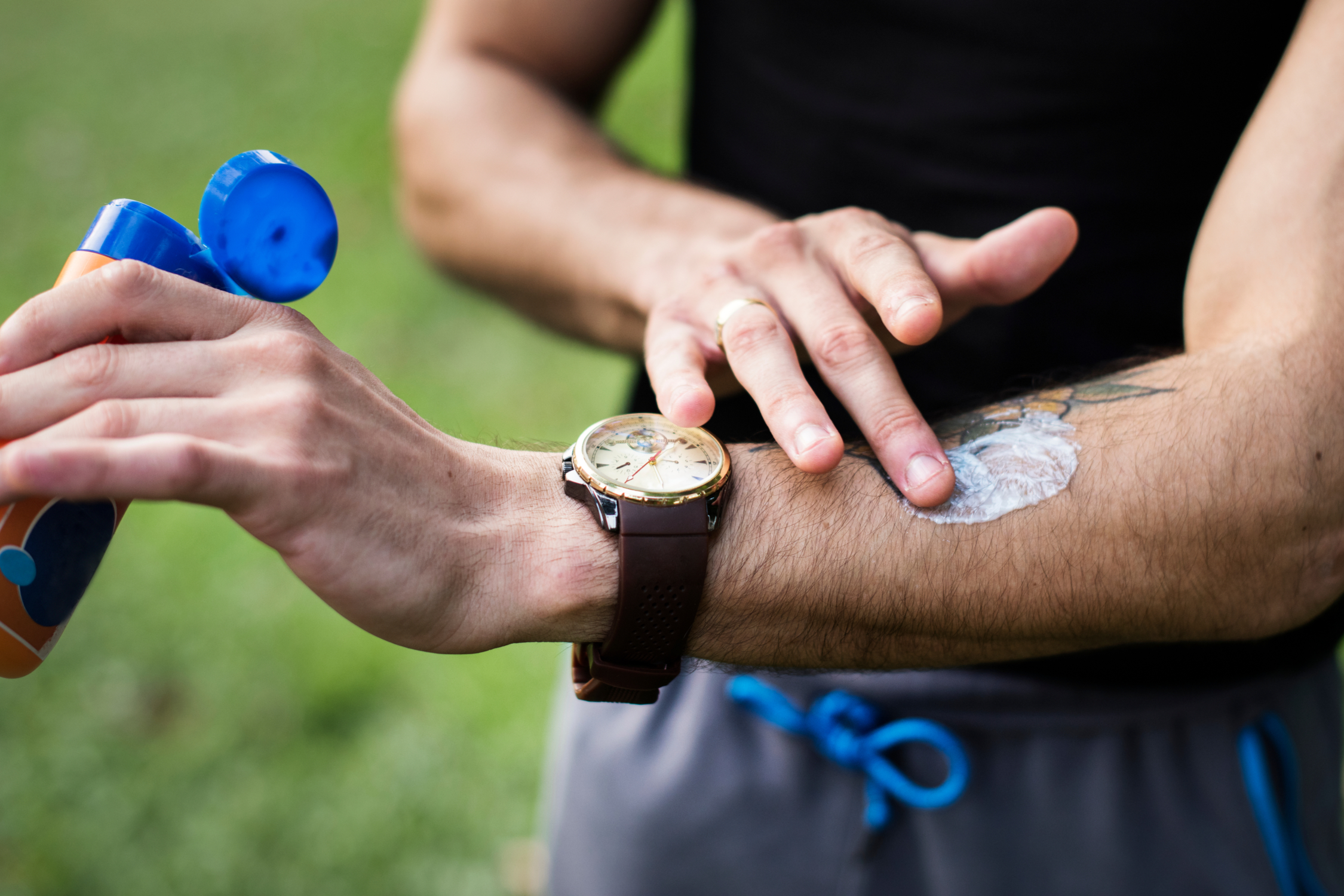 Closeup of man applying sunscreen to his arm outside in the grass