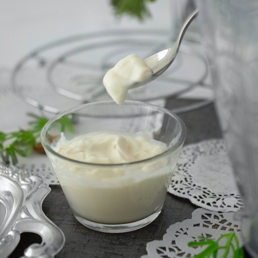 a cup and spoonful of plain yogurt on a black table