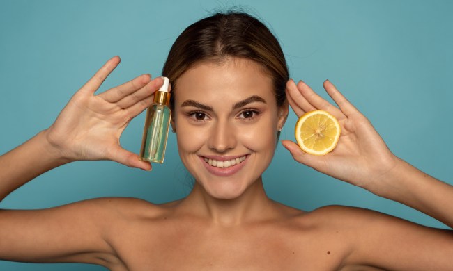 A woman holding up a serum bottle and an orange.