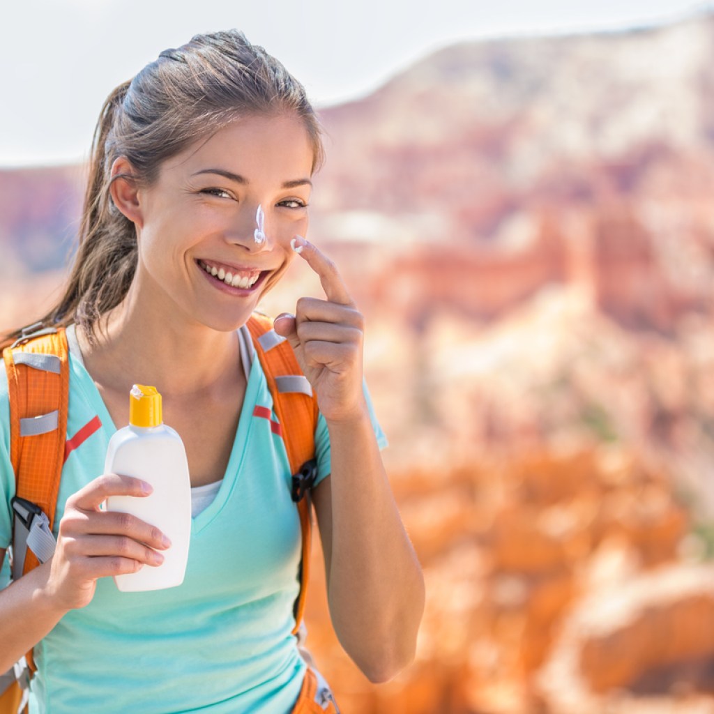 A woman putting sunscreen on her face while being out in the sun.