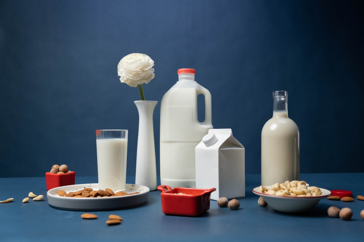 various sizes of milk containers and two bowls of nuts on a blue table with blue background