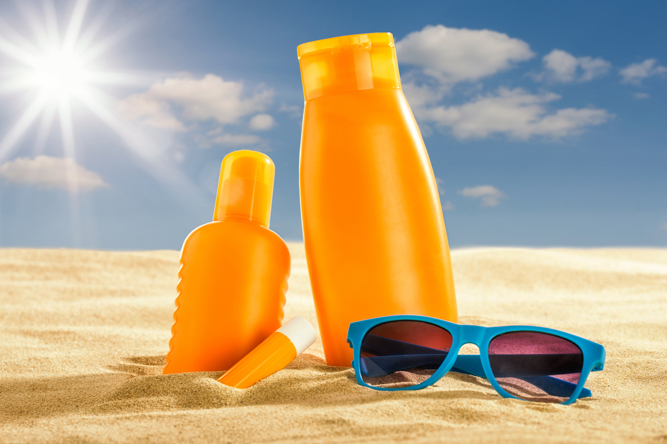 Various sunscreen products and sunglasses in the sand