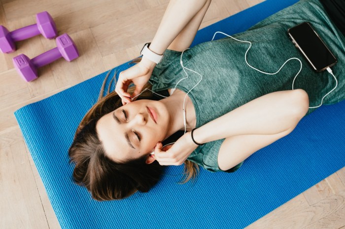 woman listening to music on blue yoga mat with purple hand weights nearby