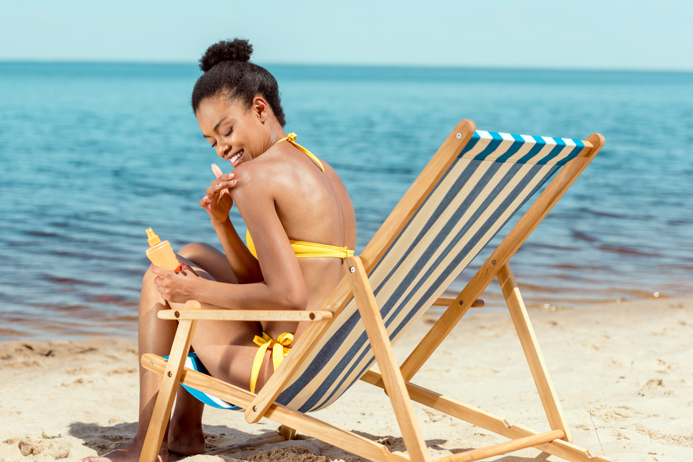 Woman sitting in beach chair applying sunscreen