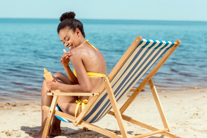 Woman sitting in beach chair applying sunscreen