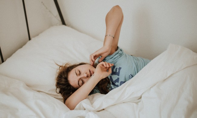 a woman sleeping towards the edge of the bed in a blue shirt