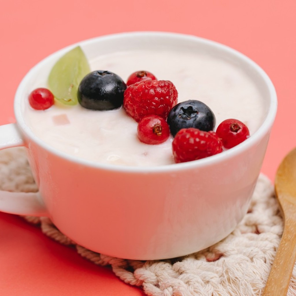 yogurt and berres in a white mug on a pink-orange background