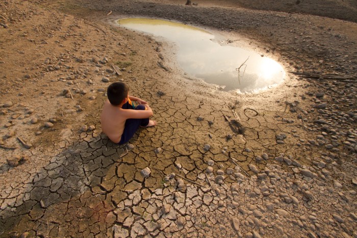 child sitting on dry, cracked ground looking at small pool of water