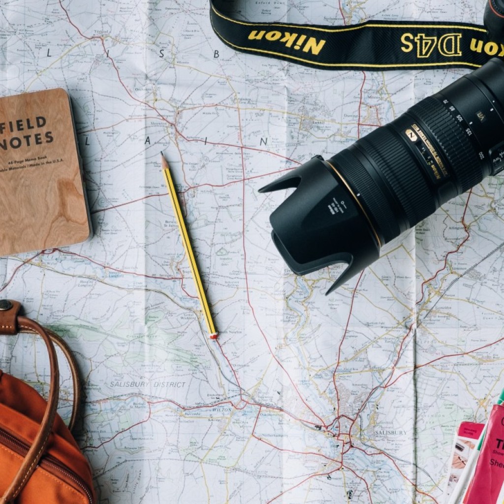 travel bag, books, camera, passport and writing instrument on top of a map