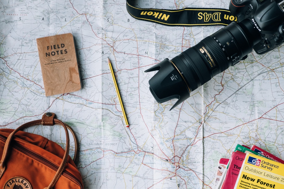 travel bag, books, camera, passport and writing instrument on top of a map