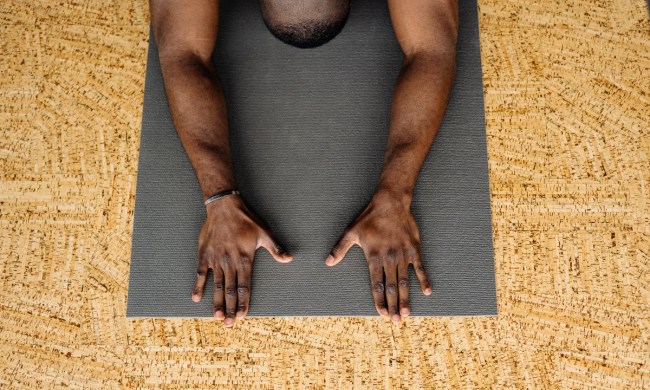 a man in child's pose on a black yoga mat