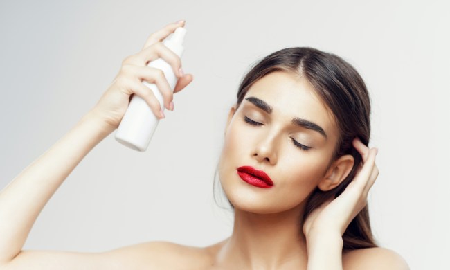 A woman spraying product into her hair.