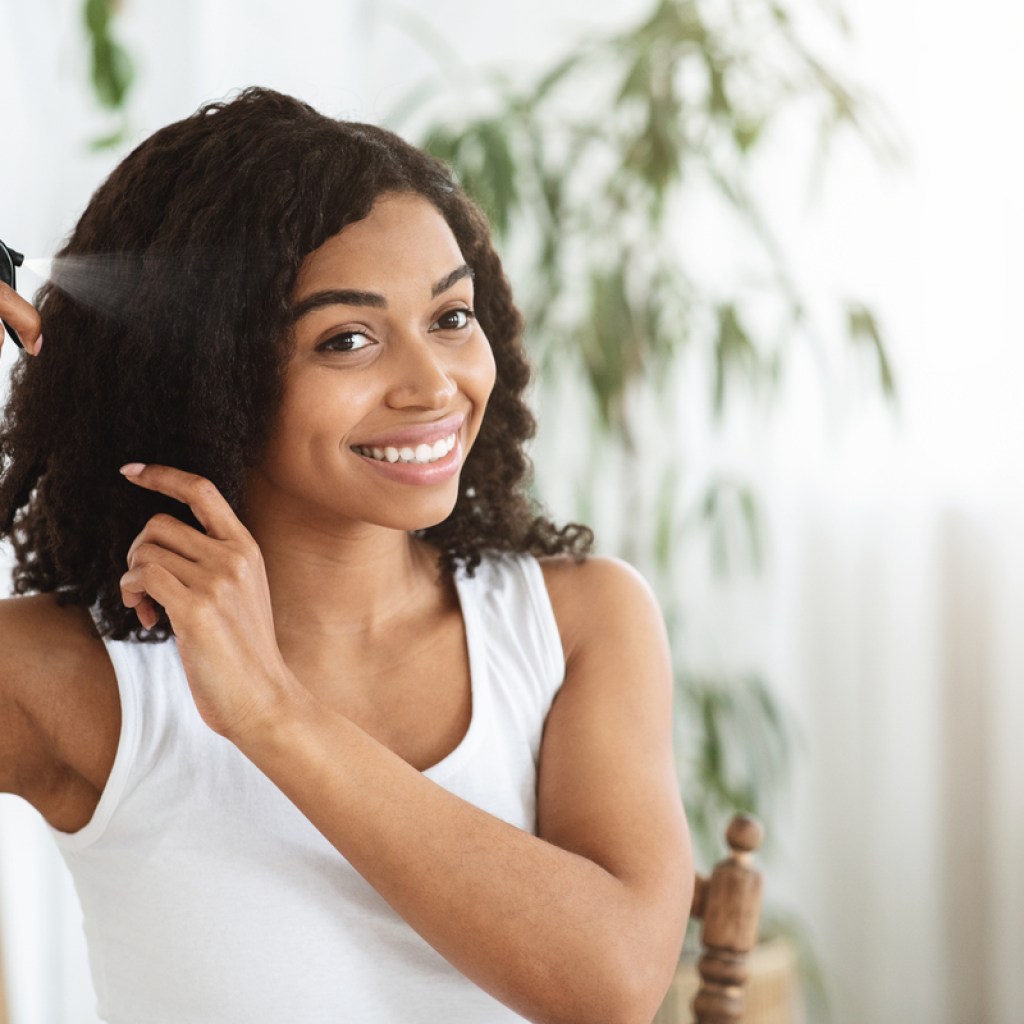 A Black woman spraying product in her hair.
