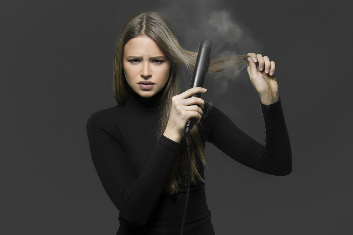 A woman taking a flat iron to her hair and smoke coming out of it.