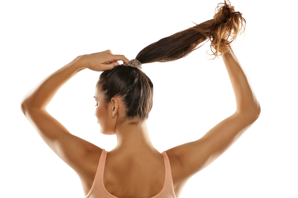 A woman putting her hair in a ponytail.