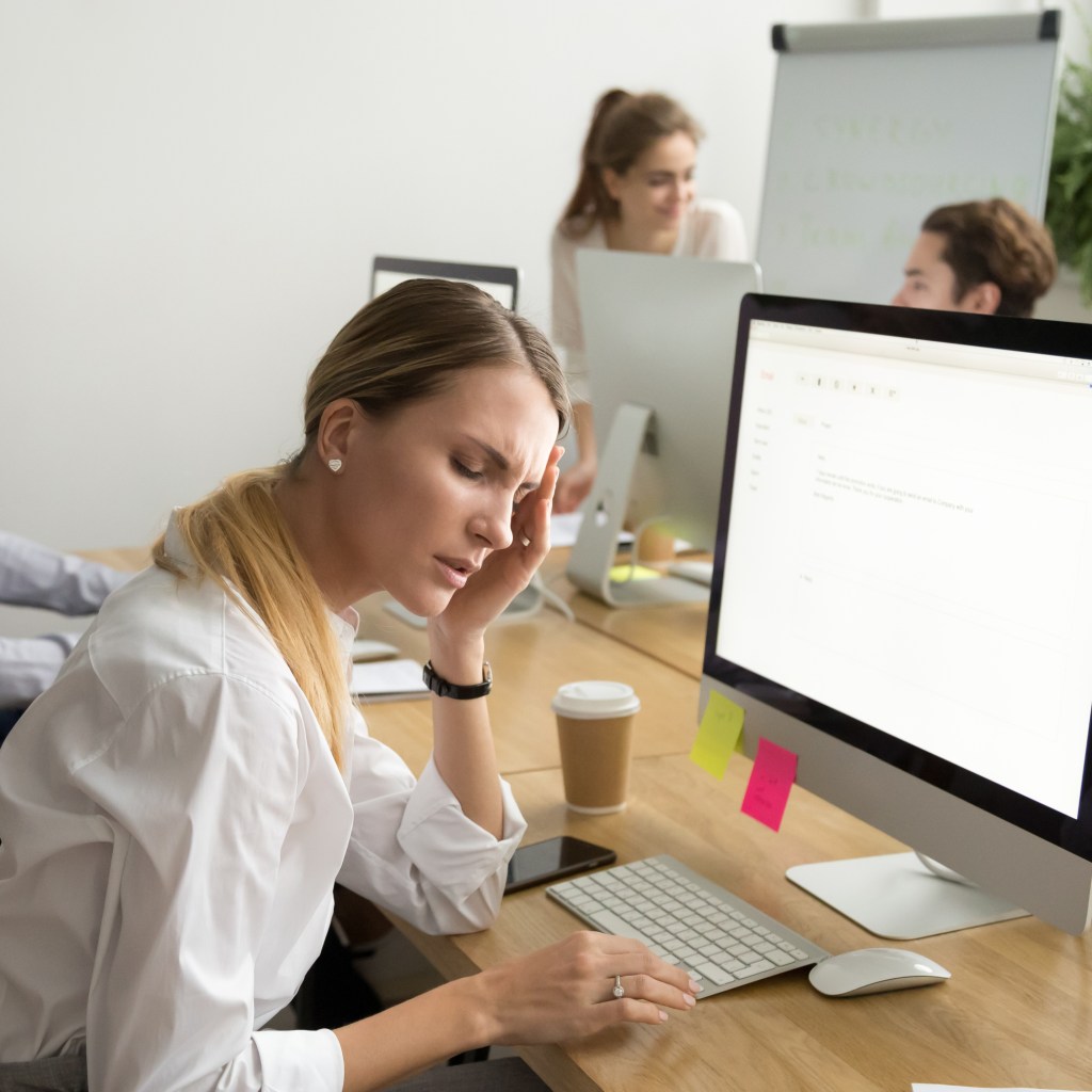 Woman in office grabbing head while working at computer