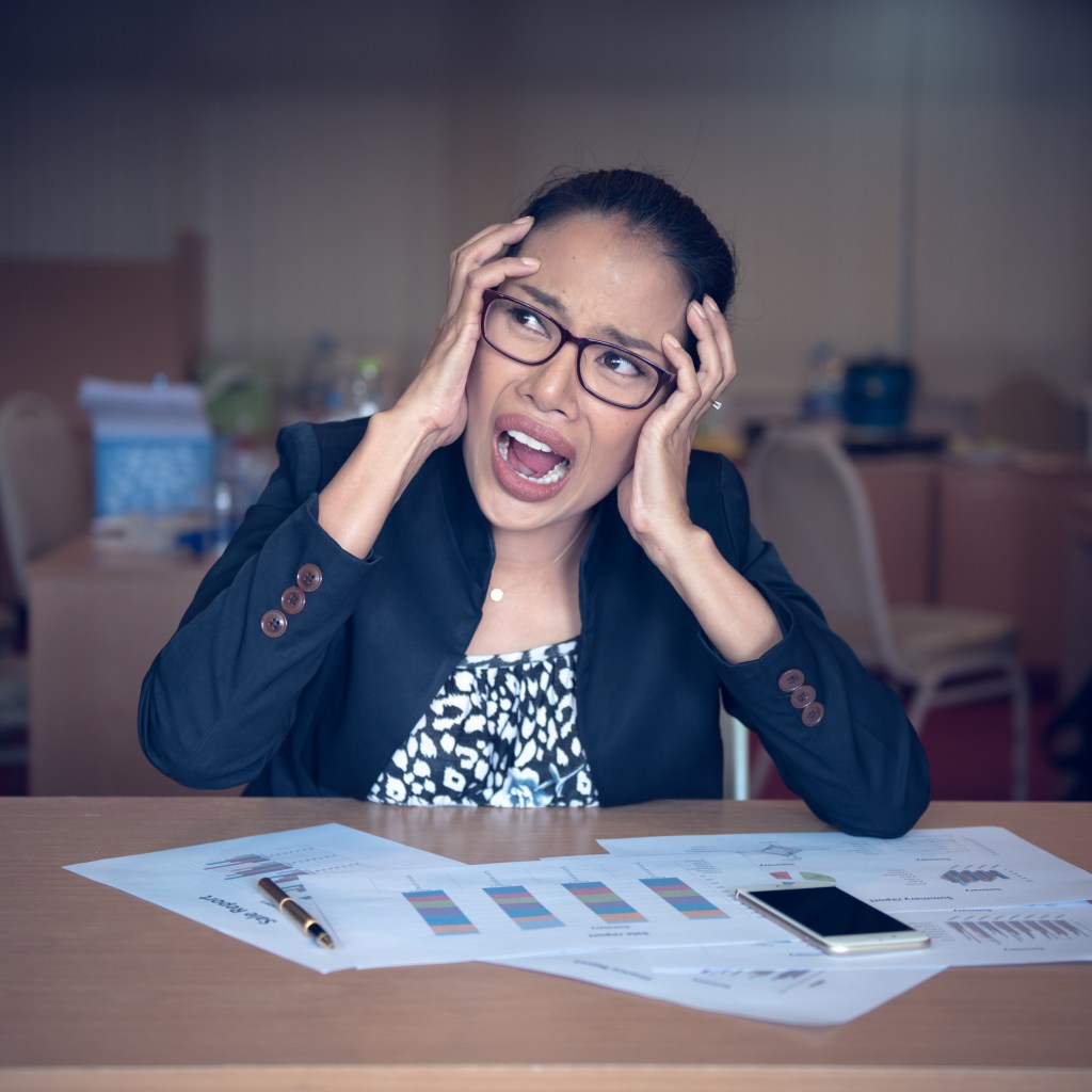 woman with work documents in front of her grabbing face and stressed