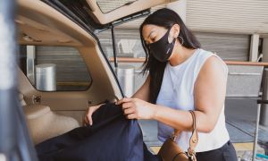 woman at airport unloading suitcase from car while wearing a mask