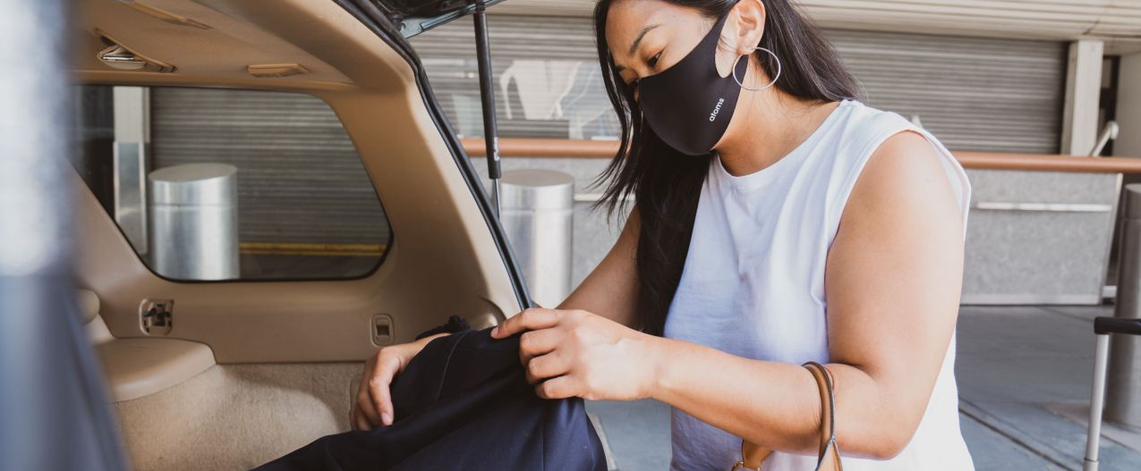 woman at airport unloading suitcase from car while wearing a mask