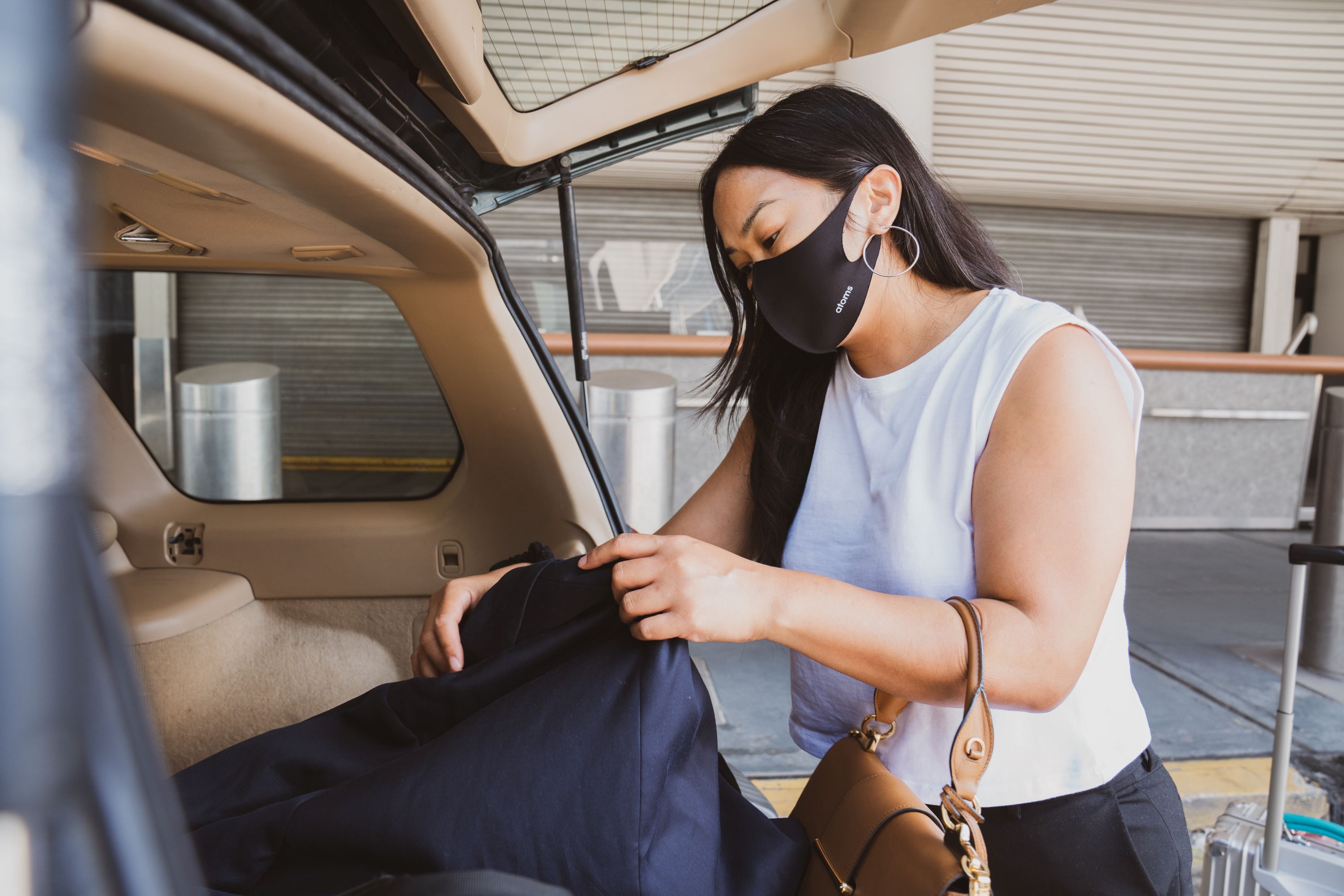 woman at airport unloading suitcase from car while wearing a mask