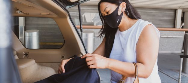 woman at airport unloading suitcase from car while wearing a mask