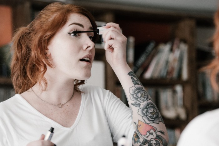 Woman with tattoos applying mascara