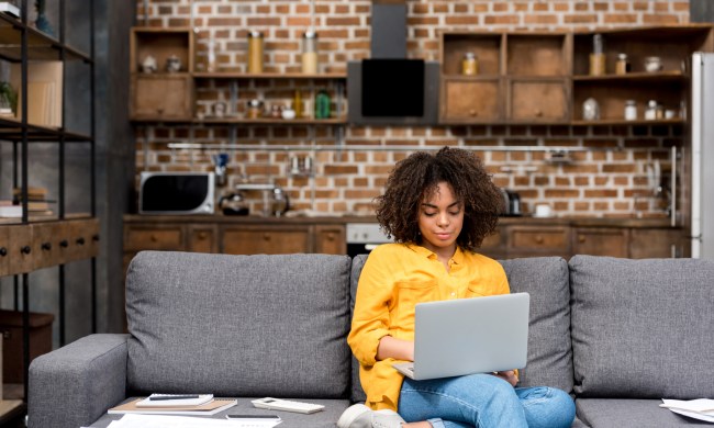 woman working while sitting on couch with laptop on lap