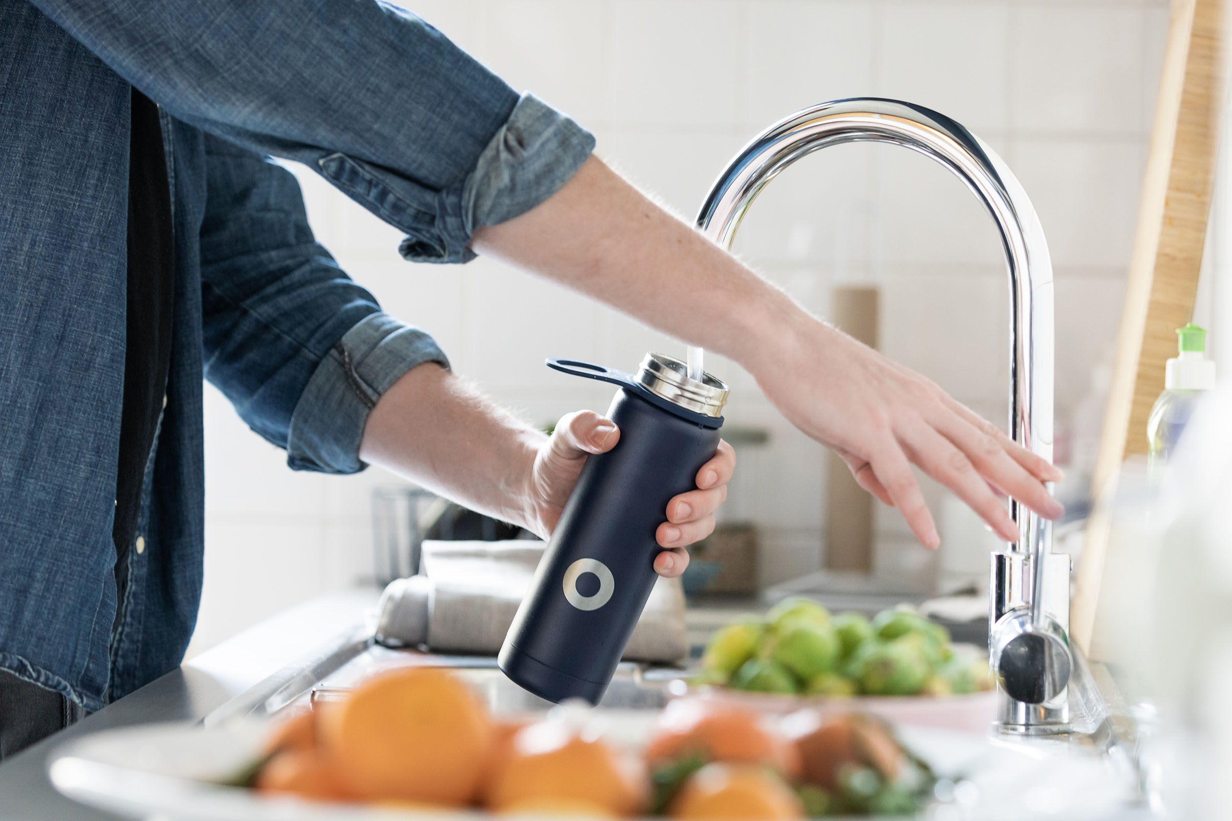 Person filling a reusable water bottle in the sink