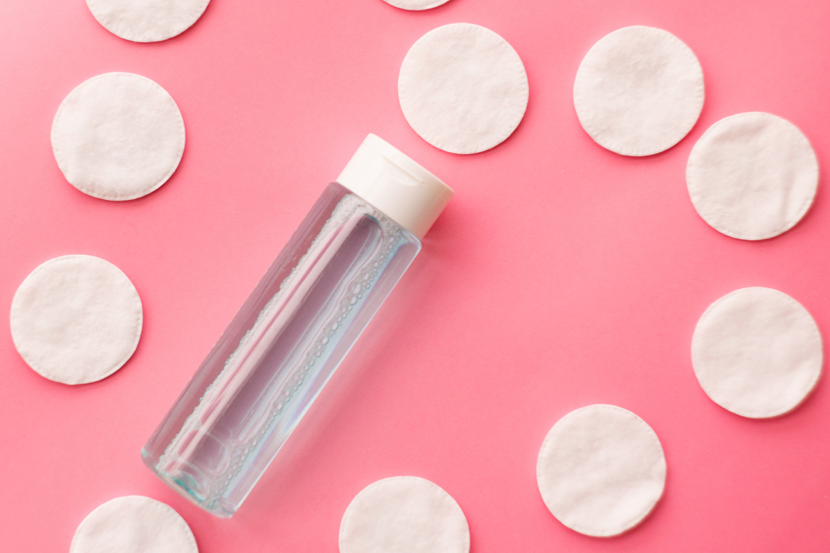 Face toner and cotton pads on a pink background.